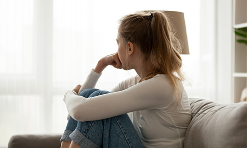 Jeune femme sur un canapé regardant pensivement par la fenêtre